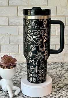 a black and gold travel mug sitting on top of a counter next to a potted plant