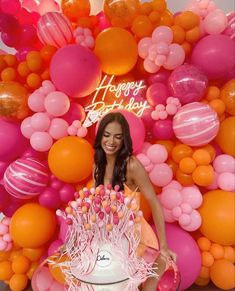 a woman standing in front of a cake surrounded by balloons and streamers with the words happy birthday written on it