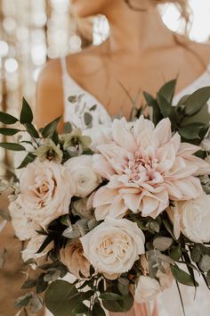 a bride holding a bouquet of white and pink flowers with greenery in her hand