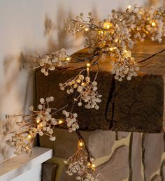 a branch with white flowers and lights hanging from it's branches on a fireplace mantel