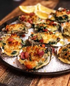 a platter filled with oysters on top of a wooden table next to lemon wedges