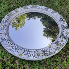 a mirror sitting in the grass with flowers on it