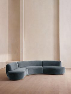 a curved couch sitting on top of a hard wood floor next to a white wall