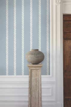 a vase sitting on top of a pedestal in front of a wallpapered room