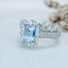 an aqua blue and white diamond ring on a white surface with other jewelry items in the background