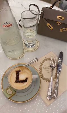 a cappuccino with the letter l on it sits next to silverware