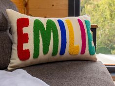 a pillow with the word emoll on it sitting on a couch in front of a window