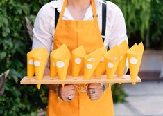 a person in an orange apron holding a tray with cones on it and smiling at the camera