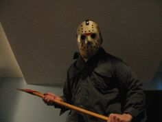 a man with a hockey mask holding a wooden stick in his hand and wearing a black jacket