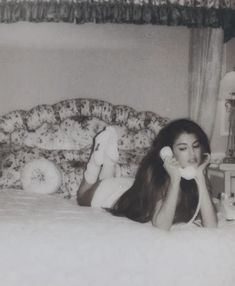 an old photo of a woman laying on her bed talking on the phone while holding a teddy bear