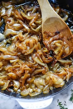 onions being cooked in a skillet with a wooden spoon