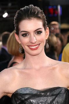 a woman in a strapless dress smiling at the camera with other people behind her