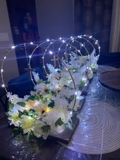 white flowers are arranged on a table with lights in the corner and around it is a circular metal stand