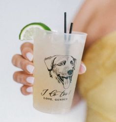 a person holding a drink with a dog on it and a lime wedge in the cup