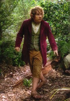 a man is walking through the woods with his foot in the air and wearing a purple coat