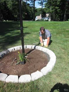 a man kneeling down next to a tree in a yard with dirt on the ground