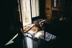 a naked woman laying on top of a bed next to a table and window in a dark room