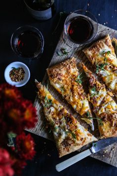 sliced pizza sitting on top of a wooden cutting board next to bowls of sauces