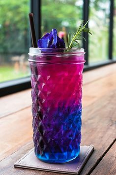 a purple and blue drink sitting on top of a wooden table next to a window