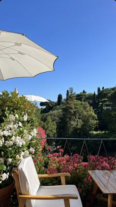 two chairs and an umbrella on a patio with flowers in the foreground, and trees in the background