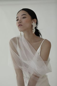 a woman in a white dress with sheer fabric on her shoulder and large flower earrings