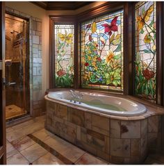 a bath tub sitting next to a window with stained glass panels on the windowsill