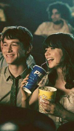 a man and woman sitting next to each other at a movie theater with popcorn in their mouths