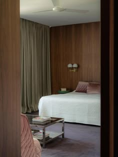 a bed sitting next to a wooden wall in a bedroom under a window with green drapes