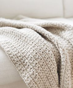 a crocheted blanket is folded on top of a white couch with pillows in the background