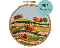 an embroidery pattern with trees and hills in the background, on a wooden hoop frame