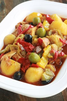 a white bowl filled with stew and olives on top of a wooden table next to a fork