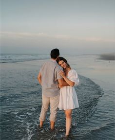 a man and woman are standing in the water at the edge of the beach together