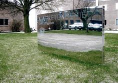 a large mirror sitting in the middle of a grass covered field next to a building