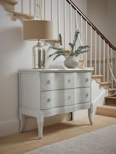 a white dresser with two vases on top of it next to a stair case