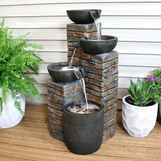 an outdoor fountain with water running from it's sides and two potted plants next to it