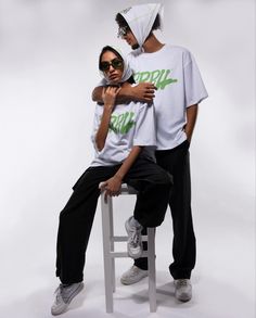 two people in white shirts and black pants sitting on a stool with their arms around each other