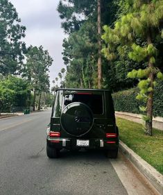 a black mercedes benz parked on the side of the road in front of some trees