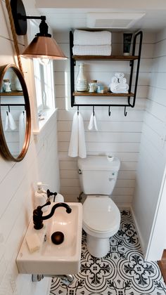 a white toilet sitting next to a sink in a bathroom under a mirror and shelf