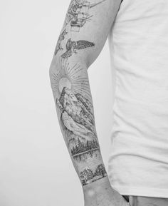 a man's arm with tattoos on it and an airplane flying over the mountains