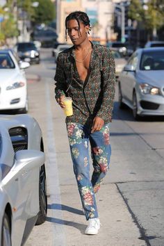 a man with dreadlocks walking down the street while holding a coffee in his hand