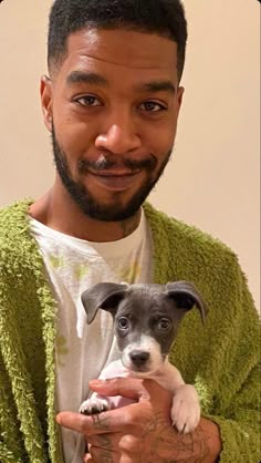 a man holding a small dog in his arms while wearing a green sweater and white t - shirt