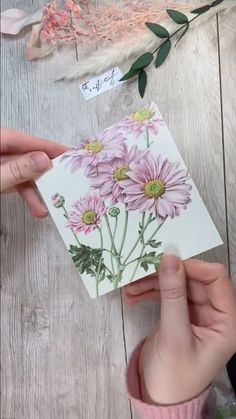 someone is holding up a card with pink flowers on it and some feathers in the background