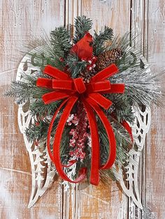 a christmas wreath hanging on the side of a wooden door with red bows and pine cones