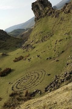 a grassy hill with rocks and grass in the foreground, on which there is a spiral design