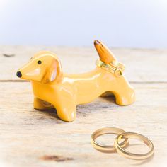 a yellow dog figurine sitting next to two wedding rings