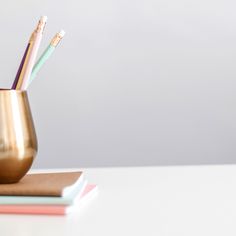 three pencils are in a gold cup on a white table