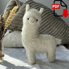 an alpaca stuffed animal next to a vase with dried flowers on a bed