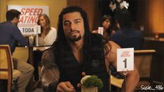 a man with long hair sitting at a table in front of a sign that says speed eating today