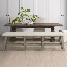 a dining room table and bench with plants in the vases on each end, along with white chairs