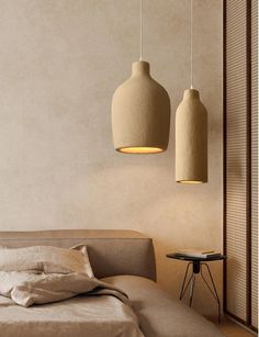 two lamps hanging from the ceiling above a bed in a room with beige walls and pillows